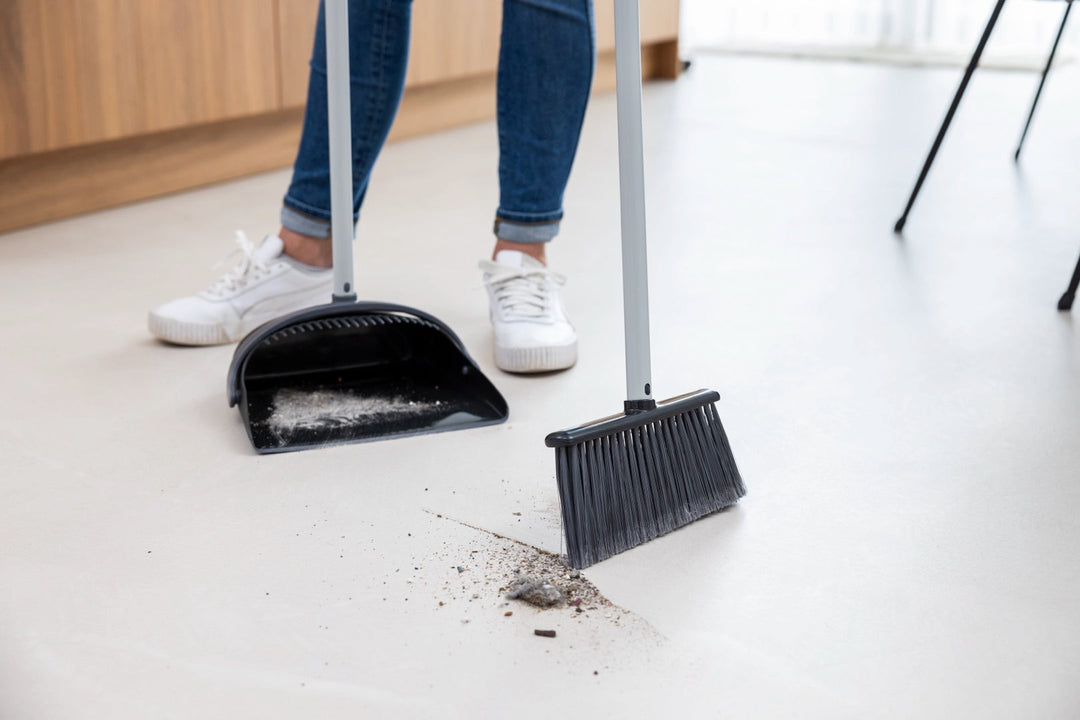 Person sweeping dust into a dustpan with a broom indoors, showcasing an efficient cleaning tool for household use