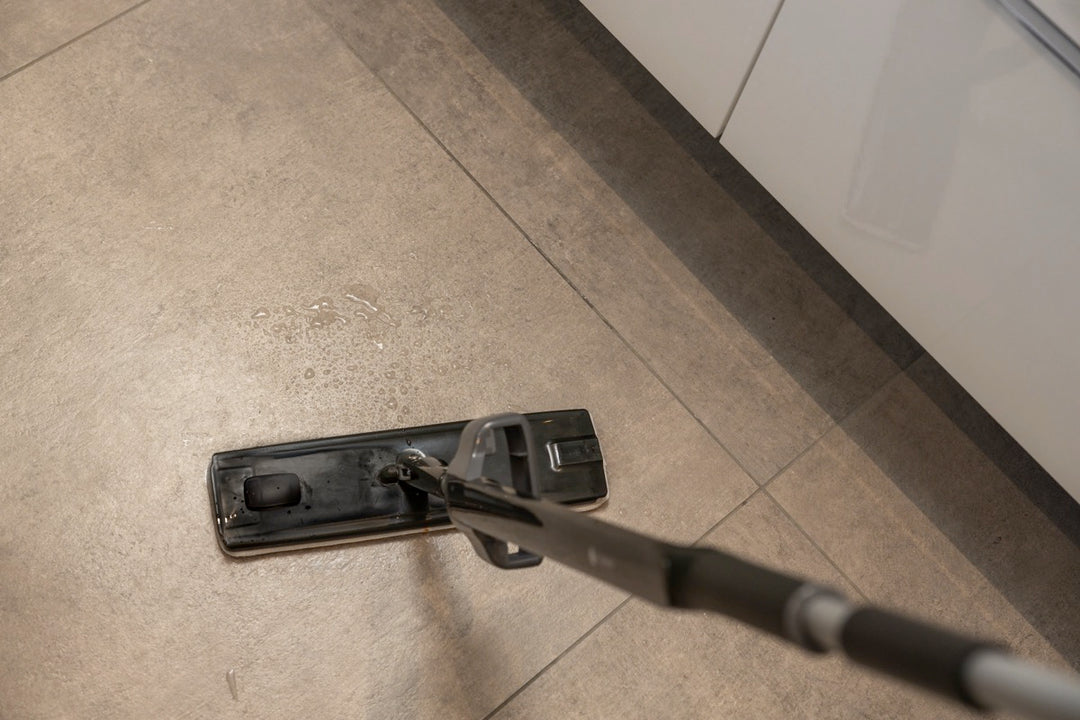 A flat mop cleaning a tiled floor, with water droplets visible on the surface