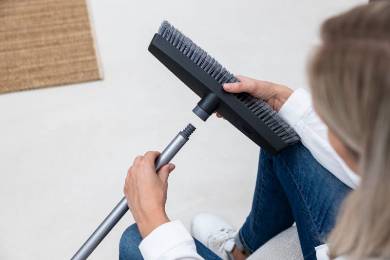 Woman assembling a broom by attaching the handle to the brush head