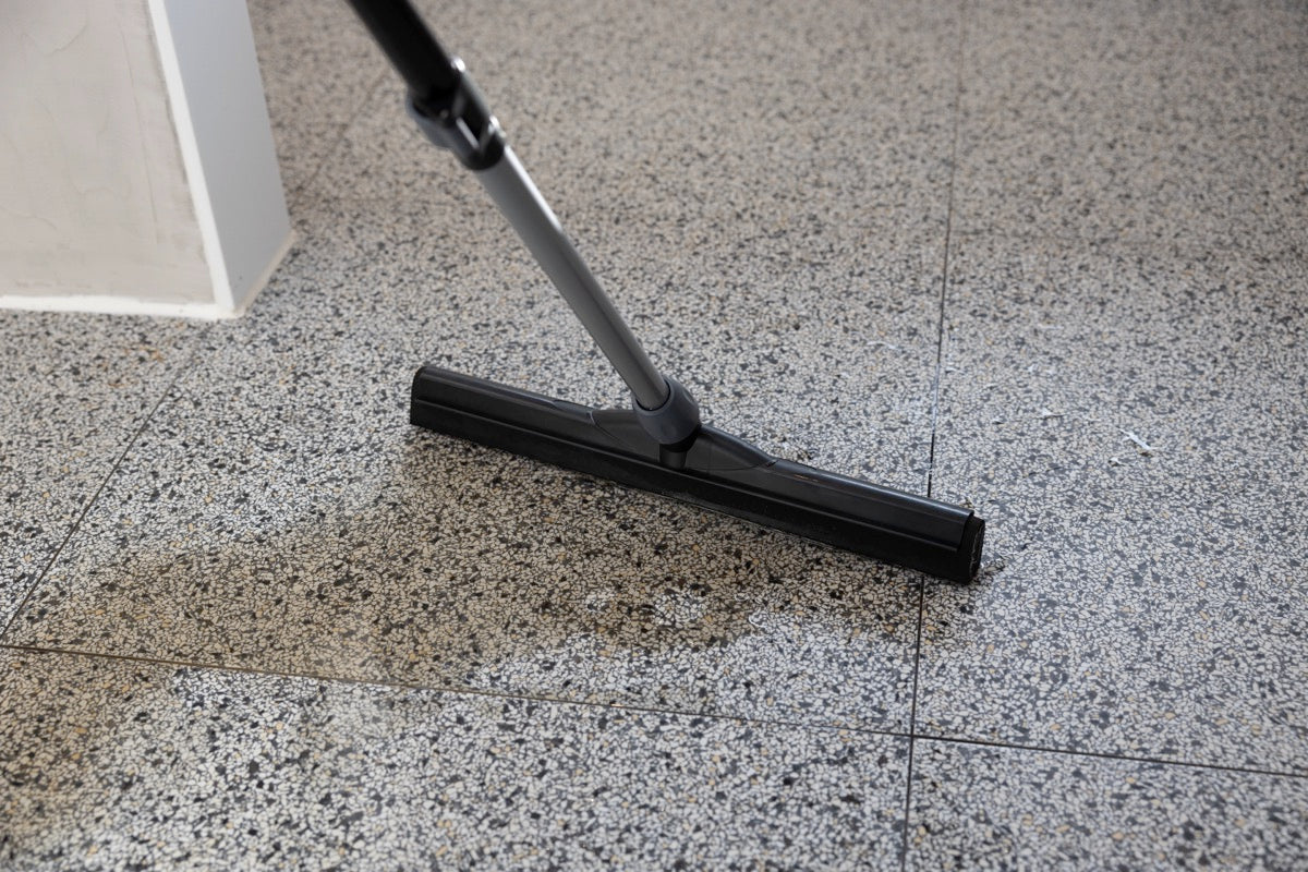 Close-up of the cleanly floor squeegee with double EVA foam on a speckled tile floor, removing water