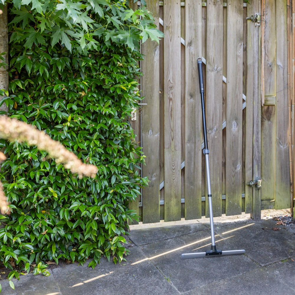 Floor squeegee leaning against a wooden fence in an outdoor garden setting