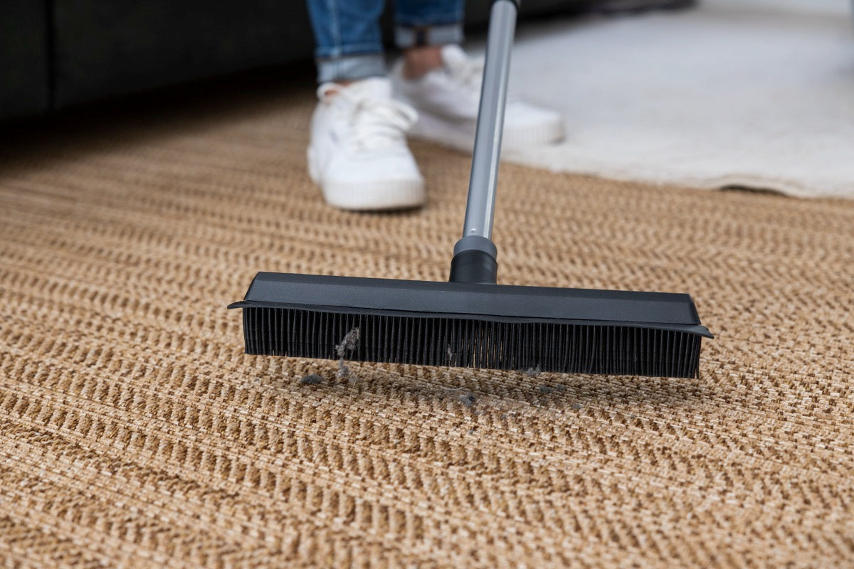 Rubber broom collecting dust and hair from a textured carpet