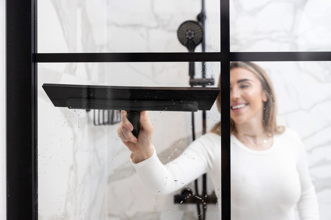 Woman using a squeegee to clean a glass shower partition