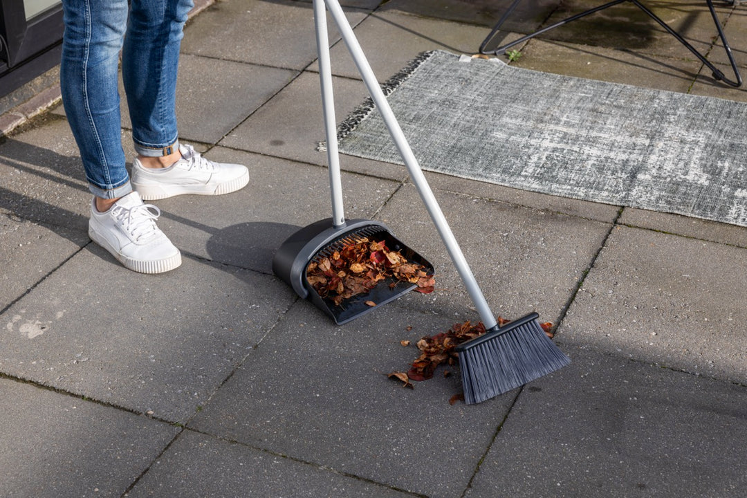 Person using a broom and dustpan to sweep leaves and debris outdoors, highlighting outdoor cleaning efficiency